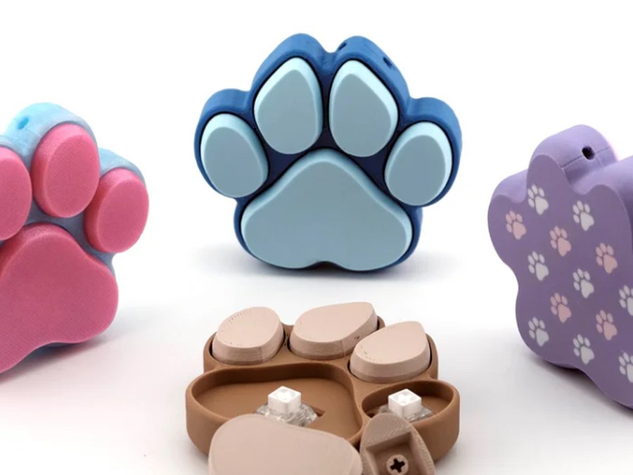 3D printed paw print fidget clickers in blue, pink and purple, one opened to show the clicker inside
